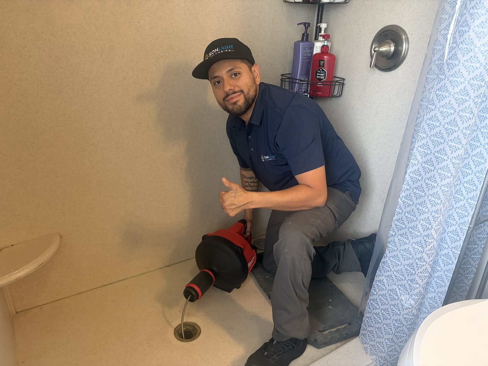 Jose from Sonlight Plumbing kneeling beside a drum machine with its cable fed into a shower drain during a Richland drain-cleaning job.